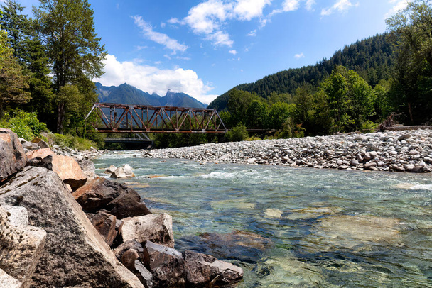 Flowing Skykomish river with cascade mountains and old bridge in background during summer time from Washington State of the pacific northwest United States - Photo, Image