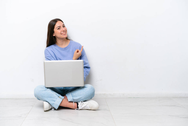 白い背景に隔離された床に座っているノートパソコンを持つ若い白人女性 - 写真・画像