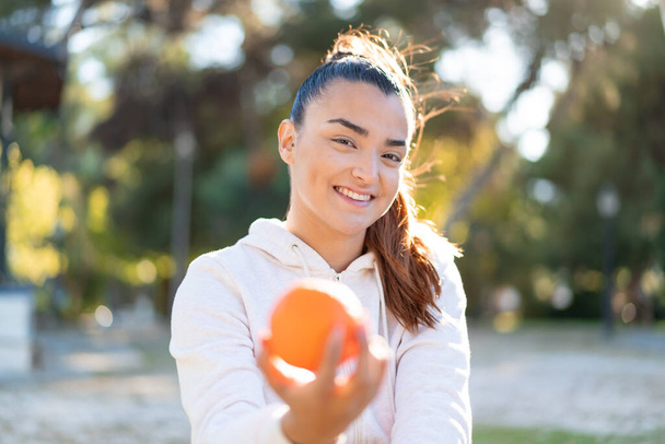 Jovem morena bonita segurando uma laranja ao ar livre com expressão feliz - Foto, Imagem