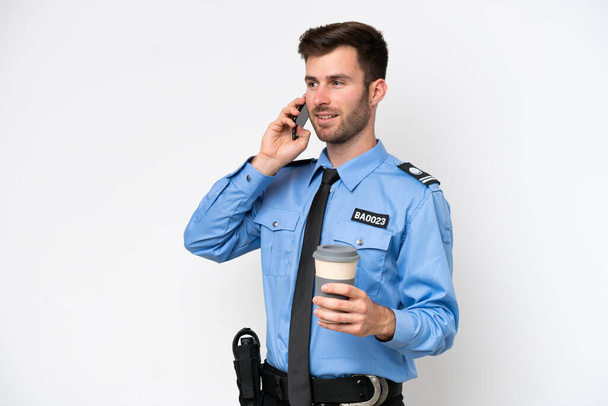 Young police caucasian man isolated on white background holding coffee to take away and a mobile - Foto, imagen