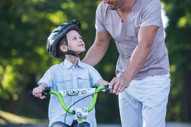 Cropped image of handsome father teaching his cute little son riding bike in park. Both are smiling - Photo, Image