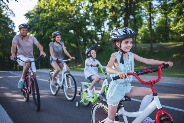 La familia feliz está montando bicicletas al aire libre y sonriendo. Niña en primer plano
 - Foto, Imagen