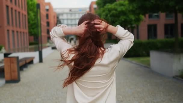 Güzel kızıl saçlı bir kadın sokakta yürüyor. Arkasını dönüp kameraya bakıyor..  - Video, Çekim