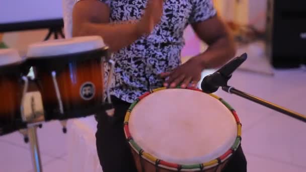 Nuori mies lyömäsoittaja, joka soittaa kuubalaisia rumpuja mustaa taustaa vasten
 - Materiaali, video