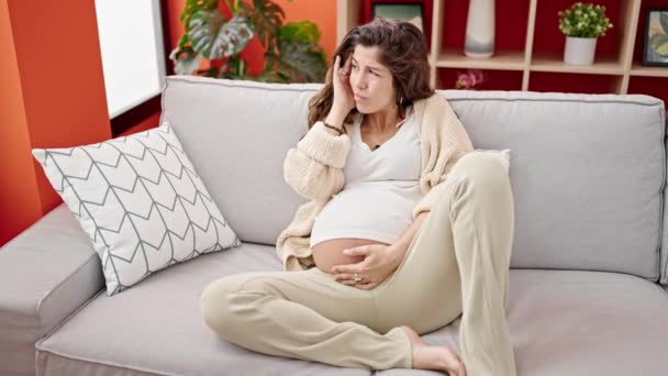 Jeune femme enceinte souffrant de maux de tête assis sur le canapé à la maison - Séquence, vidéo