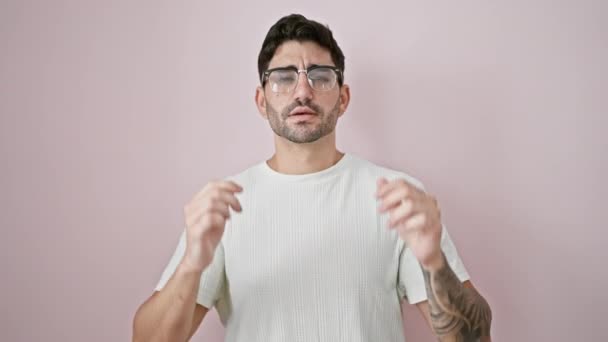 Hombre hispano joven con gafas de pie con brazos cruzados sobre fondo rosa aislado - Metraje, vídeo