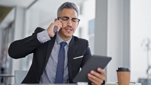 Giovane operaio ispanico uomo d'affari utilizzando touchpad parlando su smartphone in ufficio - Filmati, video