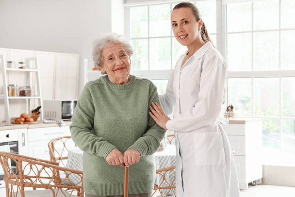 Старша жінка з ходьбою палицею і жінка-лікар на кухні - Фото, зображення