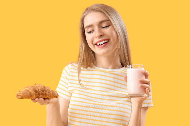 Nuori nainen maukas croissant ja jogurtti keltaisella pohjalla - Valokuva, kuva