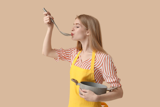 Jeune femme avec louche et casserole sur fond beige - Photo, image