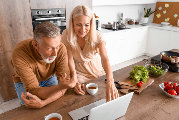 volwassen paar met laptop kijken video in keuken - Foto, afbeelding