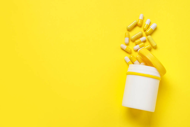 Tarro con píldoras dispersas sobre fondo amarillo - Foto, Imagen