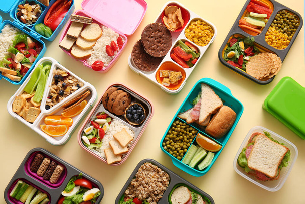 Veel lunchboxen met verschillende heerlijke gerechten op lichtgele achtergrond - Foto, afbeelding