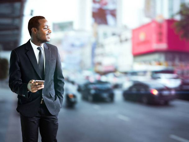 Erfolgreicher afrikanischer Geschäftsmann telefoniert außerhalb moderner Bürogebäude, Smart Mann im Business-Anzug lächelt und schaut auf Smartphone-Bildschirm SMS - Foto, Bild