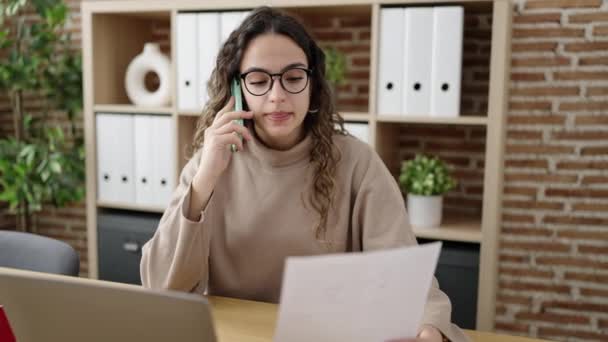 Fiatal gyönyörű spanyol nő üzleti dolgozó beszél okostelefon olvasási dokumentum az irodában - Felvétel, videó