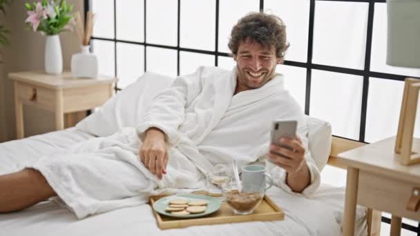 Νεαρός Ισπανός που τρώει πρωινό βλέποντας βίντεο σε smartphone στο υπνοδωμάτιο - Πλάνα, βίντεο