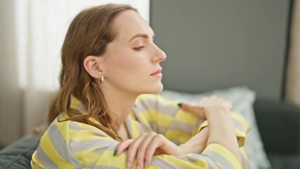 Junge blonde Frau sitzt zu Hause mit traurigem Gesichtsausdruck auf Sofa - Filmmaterial, Video