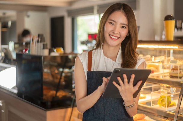 An Asian woman entrepreneur using tablet checking stock or sale income in modern coffee shop , concept small business  - Foto, afbeelding