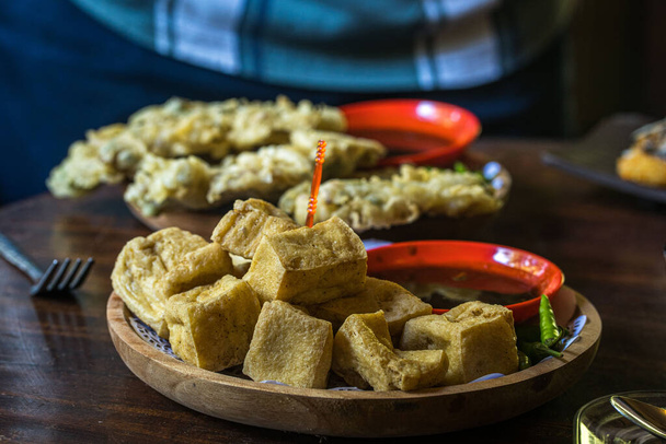 Różne smażone tofu, smażone tempeh i placki bananowe na talerzu serwowane z kawą na stole w kawiarni w Blitar, Jawa Wschodnia, Indonezja. Fotografia żywności. - Zdjęcie, obraz