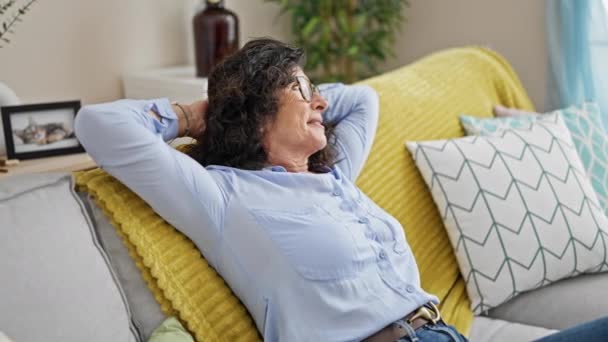 Mujer hispana de mediana edad relajada con las manos en la cabeza sentada en el sofá en casa - Metraje, vídeo