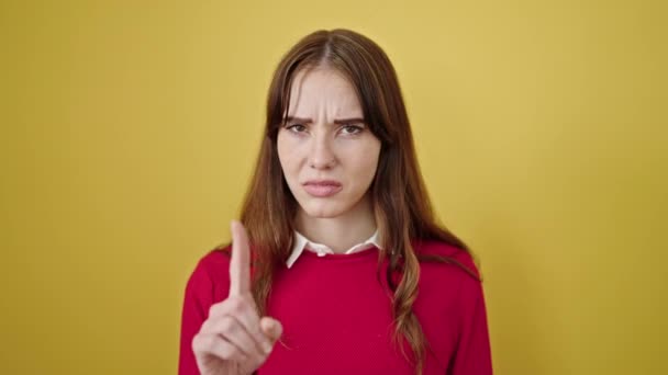 Mujer hispana joven de pie con expresión seria diciendo no con el dedo sobre el aislado fondo amarillo - Imágenes, Vídeo