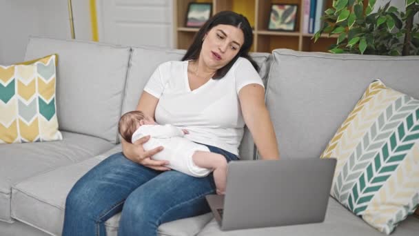 Madre e hija del bebé sentadas en un sofá sosteniendo al bebé usando un teléfono inteligente y una computadora portátil en casa - Metraje, vídeo