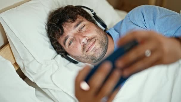 Νεαρός Ισπανός βλέπει βίντεο σε smartphone ξαπλωμένος στο κρεβάτι στο υπνοδωμάτιο - Πλάνα, βίντεο