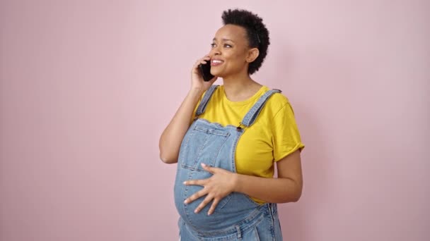 Nuori raskaana oleva nainen puhuu älypuhelimella hymyillen eristetyllä vaaleanpunaisella taustalla - Materiaali, video