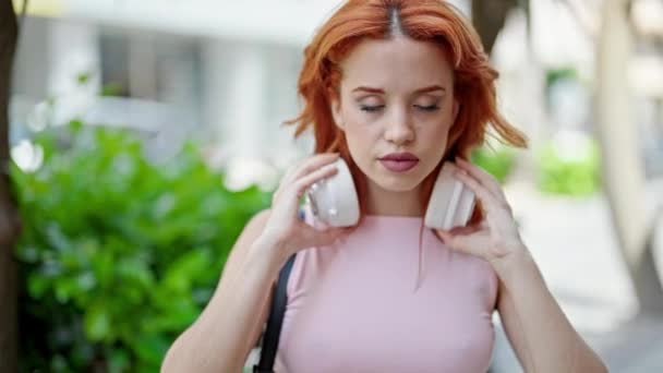 Młoda ruda kobieta wyciąga słuchawki na ulicy - Materiał filmowy, wideo