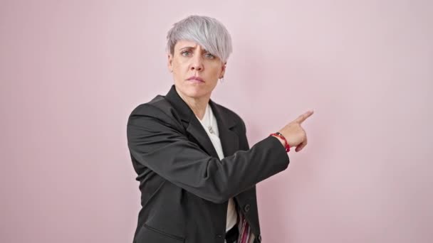 Молода жінка бізнесмен вказує на порожній простір з розлюченим обличчям над ізольованим рожевим тлом - Кадри, відео