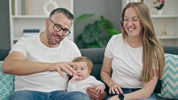 Familia de madre, padre y bebé sonriendo juntos mirando a la cámara en casa - Metraje, vídeo