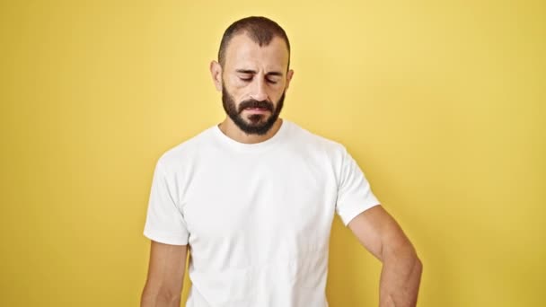 Fiatal spanyol férfi áll komoly arckifejezéssel néz elszigetelt sárga háttér - Felvétel, videó