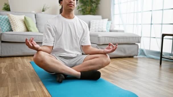 Joven latino sentado en el piso de entrenamiento de yoga en casa - Imágenes, Vídeo