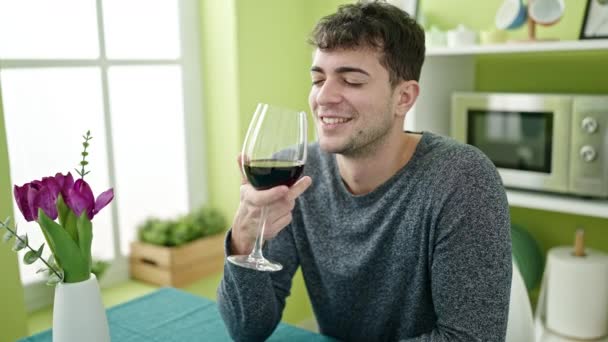 Nuori latino mies juo lasi viiniä istuu pöydällä ruokasalissa - Materiaali, video
