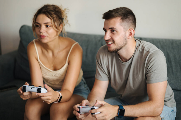 Knappe jongen met zijn verloofde die videospelletjes speelt met joysticks. De man leert haar vriendin console spelen. Hoge kwaliteit foto - Foto, afbeelding