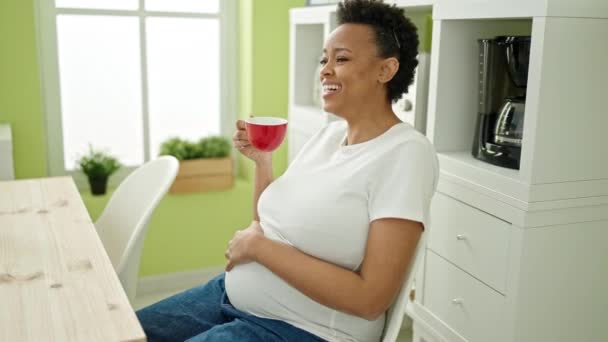 Νεαρή έγκυος γυναίκα που πίνει καφέ καθισμένη στο τραπέζι στην τραπεζαρία - Πλάνα, βίντεο