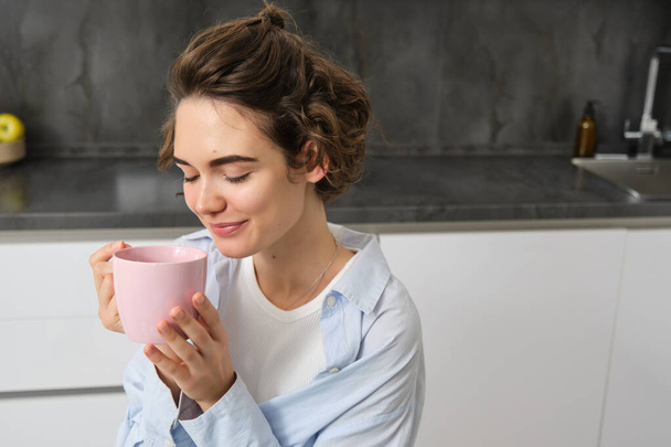 Evde kahve içen neşeli genç bir kadının portresi. Gülümseyen güzel kız sabah sıcak çay içer. Heyecanlı bir kadın güler bir sonbahar gününde. - Fotoğraf, Görsel