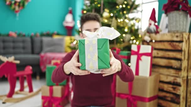 Junger hispanischer Mann hält Weihnachtsgeschenk lächelnd zu Hause - Filmmaterial, Video