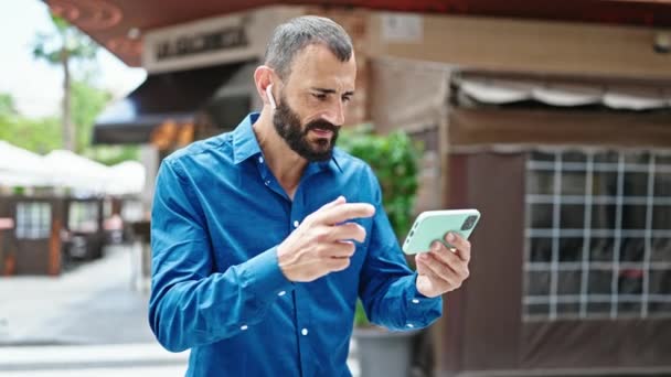 Jeune homme hispanique regarder la vidéo sur smartphone avec geste gagnant à la terrasse du café - Séquence, vidéo