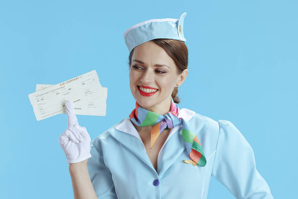 happy modern air hostess woman on blue background in blue uniform with flight tickets. - Foto, imagen