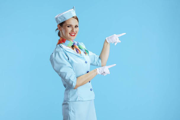 happy modern female flight attendant isolated on blue background in blue uniform pointing at something. - Fotografie, Obrázek