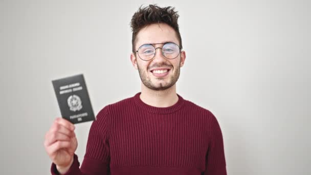 Молодой латиноамериканец улыбается уверенно держа итальянский паспорт на изолированном белом фоне - Кадры, видео