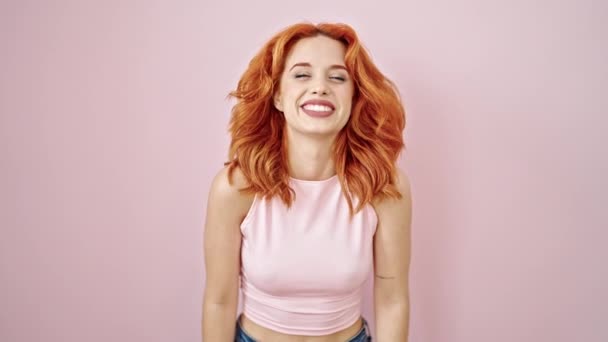 Nuori punapää nainen hymyilee luottavainen seisoo yli eristetty vaaleanpunainen tausta - Materiaali, video