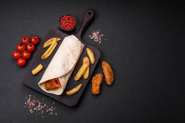 Delicious roll with chicken nuggets, tomatoes, lettuce and sauces with salt and spices on a dark concrete background - Photo, Image