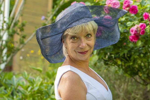 Portrait of an elderly beautiful woman wearing a fashionable ladies hat against a blurred neutral background of nature. - Photo, Image