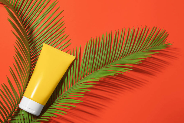 Sunscreen and tropical leaves on coral background, flat lay. Sun protection care - Foto, Imagem
