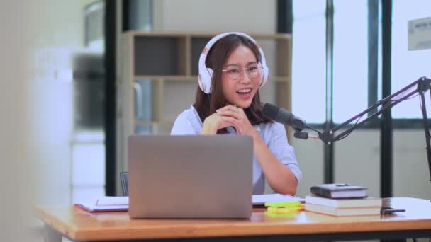 Genç Asyalı kadın sunucu ya da DJ abonelerle konuşuyor ses yayını yapıyor ya da konuşuyor ses yapıyor, mikrofon kullanıyor ve kulaklık takıyor, yayın yapıyor  - Video, Çekim