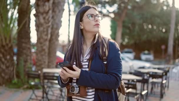 Νεαρή Ισπανίδα τουρίστρια φορώντας σακίδιο χρησιμοποιώντας smartphone στο δρόμο - Πλάνα, βίντεο