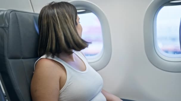 Giovane bella donna ispanica sorridente seduta a guardare attraverso la finestra in aereo - Filmati, video
