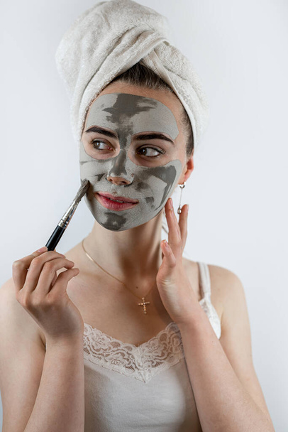 Jolie femme appliquant avec de l'argile au pinceau ou un masque facial en boue isolé sur blanc. Soins de beauté spa  - Photo, image